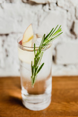 A vertical image of a refreshing gin and tonic with rosemary and apple in a highball glass. Selective focus.