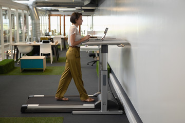 Businesswoman working on laptop while doing exercise on treadmill