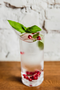 A vertical image of a refreshing gin and tonic with pomegranate and basil in a highball glass. Selective focus.