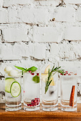 A vertical image of 4 different refreshing gin and tonics in highball glasses. Cucumber and melon,...