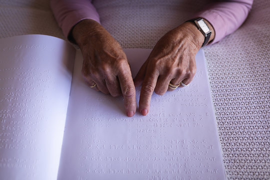 Blind active senior woman hands reading a braille book on bed in bedroom at home
