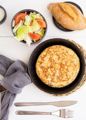 .Tortilla, Spanish omelette made with eggs and potatoes on wooden table. Traditional Spanish tapas or snack served with salad and bread.