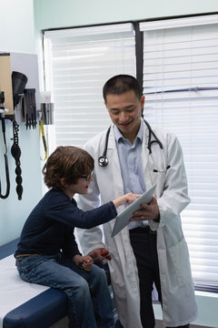 Young asian male doctor and caucasian boy patient using digital tablet in the clinic