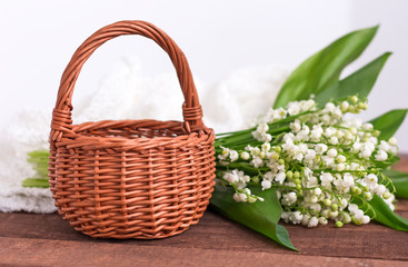 Fototapeta na wymiar bouquet of white lilies of the valley with a wicker basket on a brown wooden background and delicate fabric