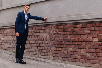 young stylish guy with a monumental face walks in a cool city near the wooden and stone walls