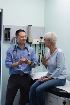 Young Asian male doctor and senior patient discussing over heart model 