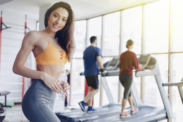 young attractive girl in the gym drinking water on the background of treadmills