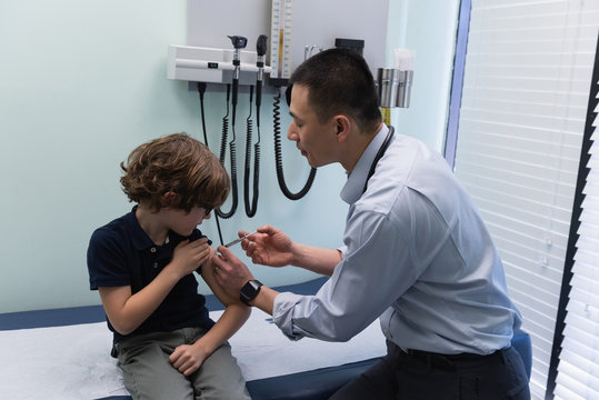 Young asian male doctor injecting syringe to caucasian boy patient in clinic