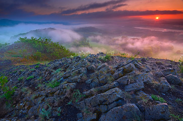 Magic dark basalt poles on peak above misty valley after daybreak.