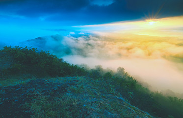Sunrise on top of rocky mountain with view into misty valley.