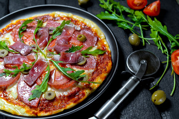 pizza with prosciutto olives and arugula on a black background