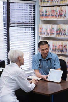 Young Asian male doctor and senior patient discussing over digital tablet in the clinic 
