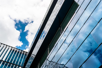 The facade of a modern building made of glass, blue panels in which the sky is reflected.