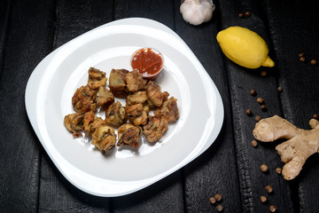 fried rapana with sauce in a white plate on a black background