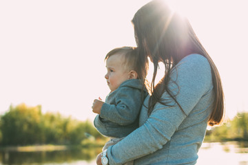 Happy woman with Cute baby boy on hands on lake water background outdoors, sensitivity to nature...