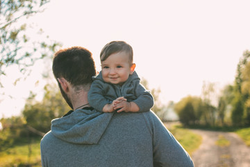 Cute baby boy on his dad's shoulders walking on the road outdoors, sensitivity to nature concept