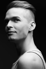 Portrait of smiling handsome young man in casual gray sleeveless shirt posing over dark gray background. Perfect hair and skin. Urban hipster style.  Studio shot