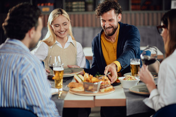 Multiethnic friends sitting at restaurant, drinking alcohol, chatting and having burgers for dinner.