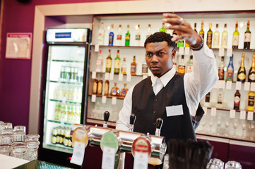 African american bartender at bar pouring from tap fresh beer into the glass in pub.