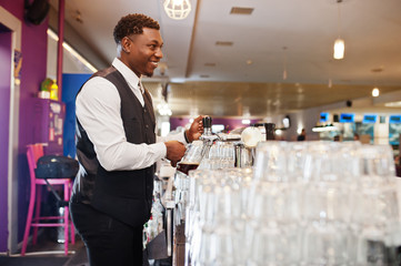 African american bartender at bar pouring from tap fresh beer into the glass in pub.
