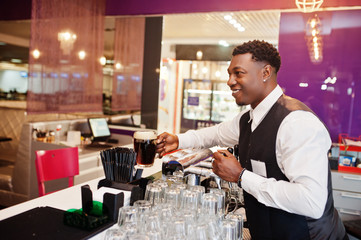 African american bartender at bar hold fresh dark beer at glass in pub.