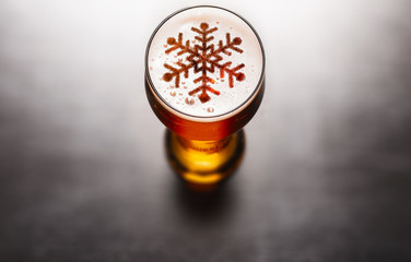 Christmas or New Year beer concept. Snow symbol on beer glass foam on black table, view from above