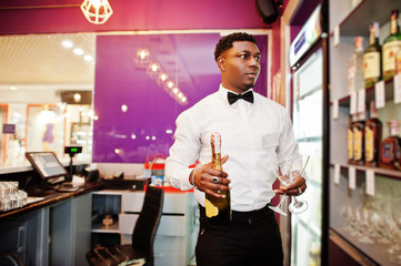 African american bartender at bar holding champagne with glasses.