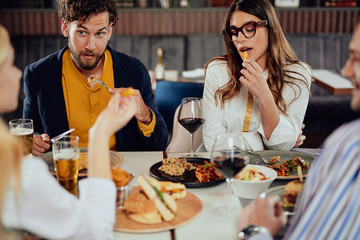 Multiethnic friends sitting at restaurant, drinking alcohol, chatting and having burgers for dinner.