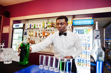 African american bartender at bar making coctails on shots. Alcoholic beverage preparation.