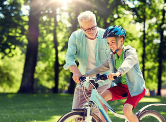 family, generation, safety and people concept - happy grandfather teaching boy how to ride bicycle...