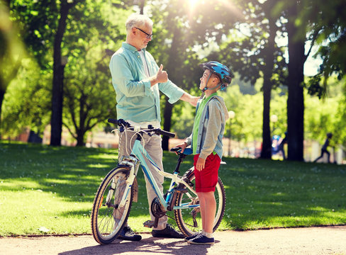 family, generation, safety and people concept - happy grandfather and boy with bicycle and bike helmet at summer park