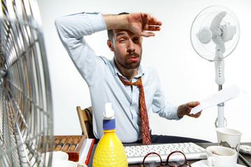 The true hell is here. Young man suffering from the heat in the office. Fans do not help, it's like...