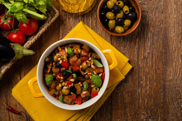Traditional Italian caponata, served with croutons in a yellow, sunny pot. Decorated with basil and pine nuts.