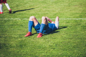 Fototapeta na wymiar Football player lying on the lawn from pain after an injury - a rough game