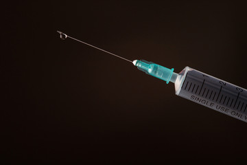 The end of the syringe with a needle filled with liquid on a dark background.