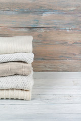 Fototapeta na wymiar Knitted wool sweaters. Pile of knitted winter clothes on wooden background, sweaters, knitwear, space for text.