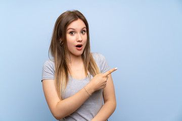 Teenager girl over isolated blue wall surprised and pointing side