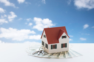 mortgage, real estate and property concept - close up of home or house model and money over blue sky and clouds background