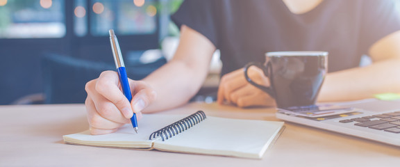 Woman hand is writing on a notebook with a pen.