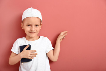 Little Muslim boy with Koran pointing at something on color background
