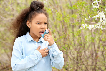 African-American girl with inhaler having asthma attack outdoors on spring day