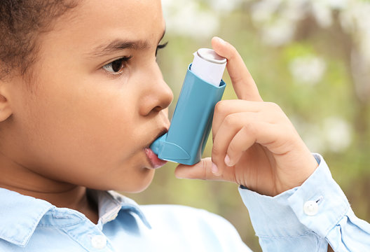 African-American girl with inhaler having asthma attack outdoors on spring day