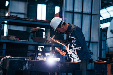 Mature man welding metal parts at heavy industry factory, side view.