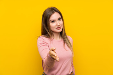 Teenager girl over isolated yellow background handshaking after good deal