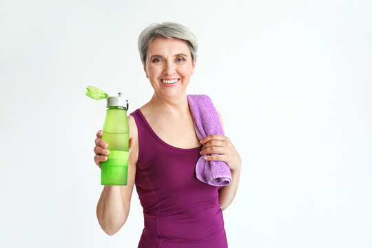 Sporty mature woman with bottle of water and towel on white background