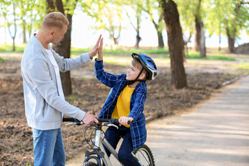 Fototapeta premium Father giving his little son high-five while teaching him to ride bicycle outdoors