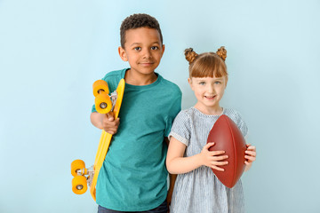 Cute little children with skateboard and rugby ball on color background