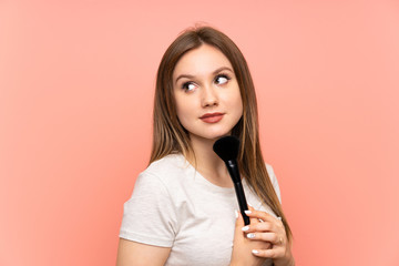 Teenager girl over pink background with makeup brush