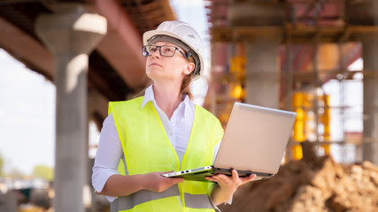 Portrait of engineer woman working on laptop on background of construction overpass.