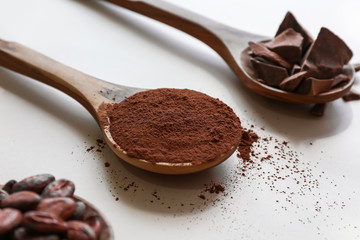 Spoons with cocoa powder, beans and chocolate on white background